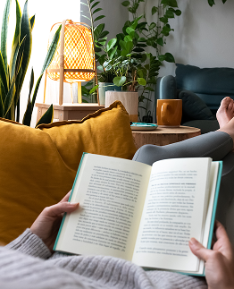 First person view of a person reclined on a sofa with their feet up reading a book