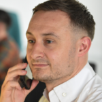 Office worker taking a phone call, wearing a white shirt, with a blurred office background.